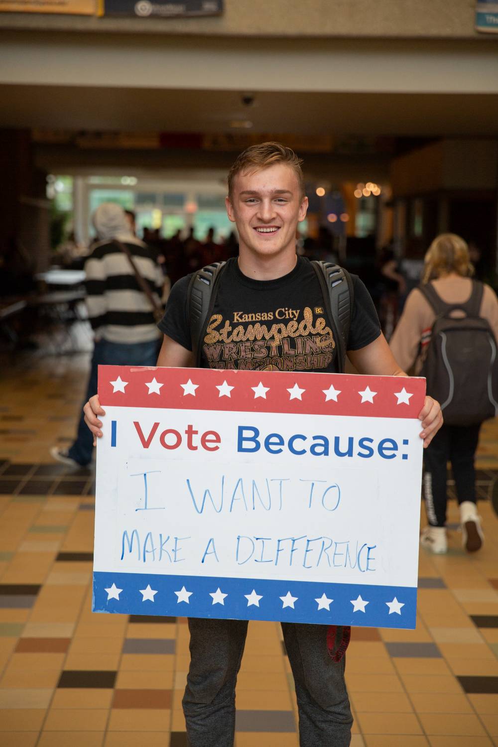 Student holding sign titled "I vote because: I want to make a difference"